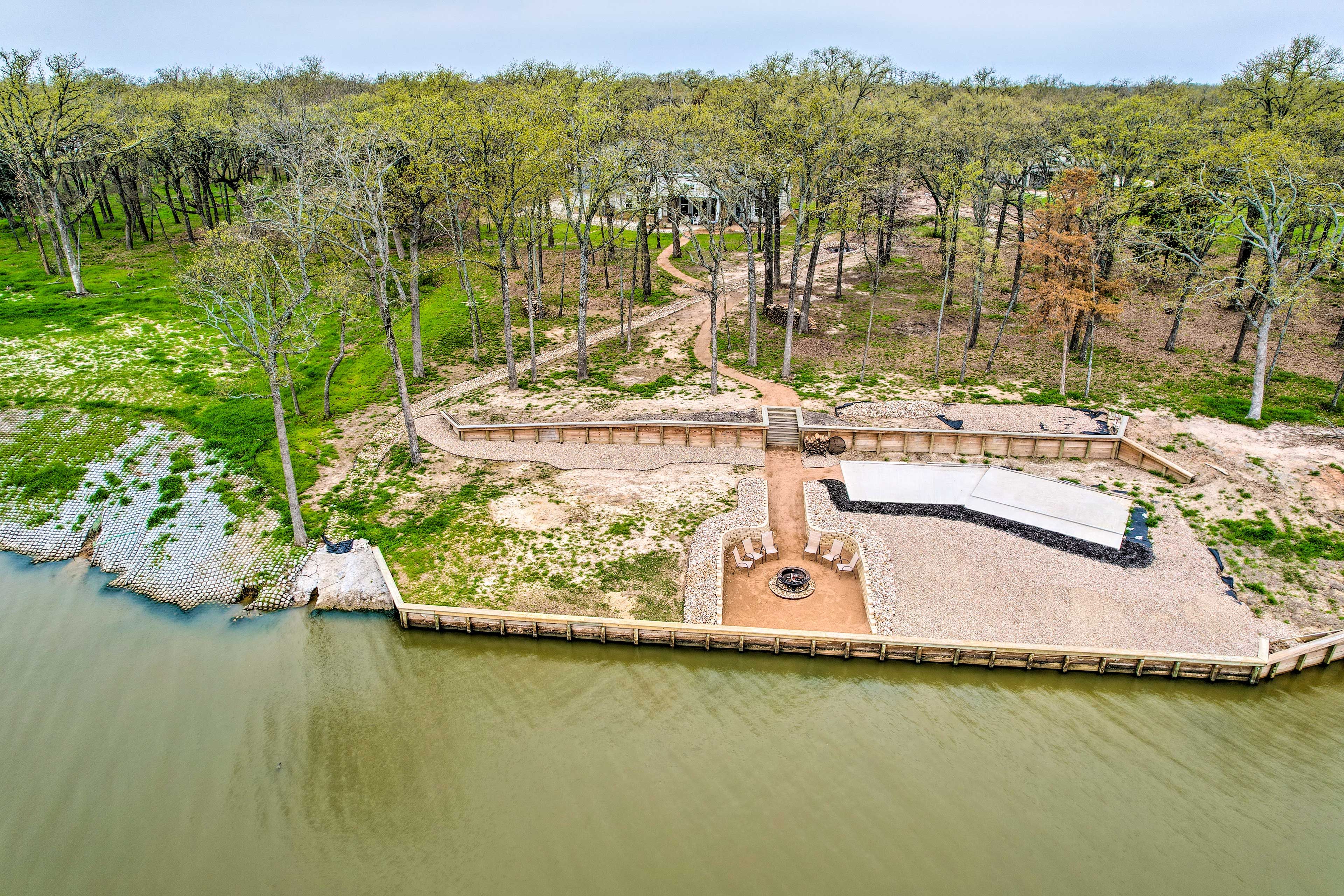 An aerial view of a park with a dock extending into a body of water, surrounded by trees and a walking path.