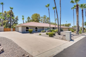 A single-story house with a red-tiled roof, a front entrance with a wooden door, and a driveway leading to the garage. - Pool, Hot Tub: Family-friendly Scottsdale Home! (Scottsdale)