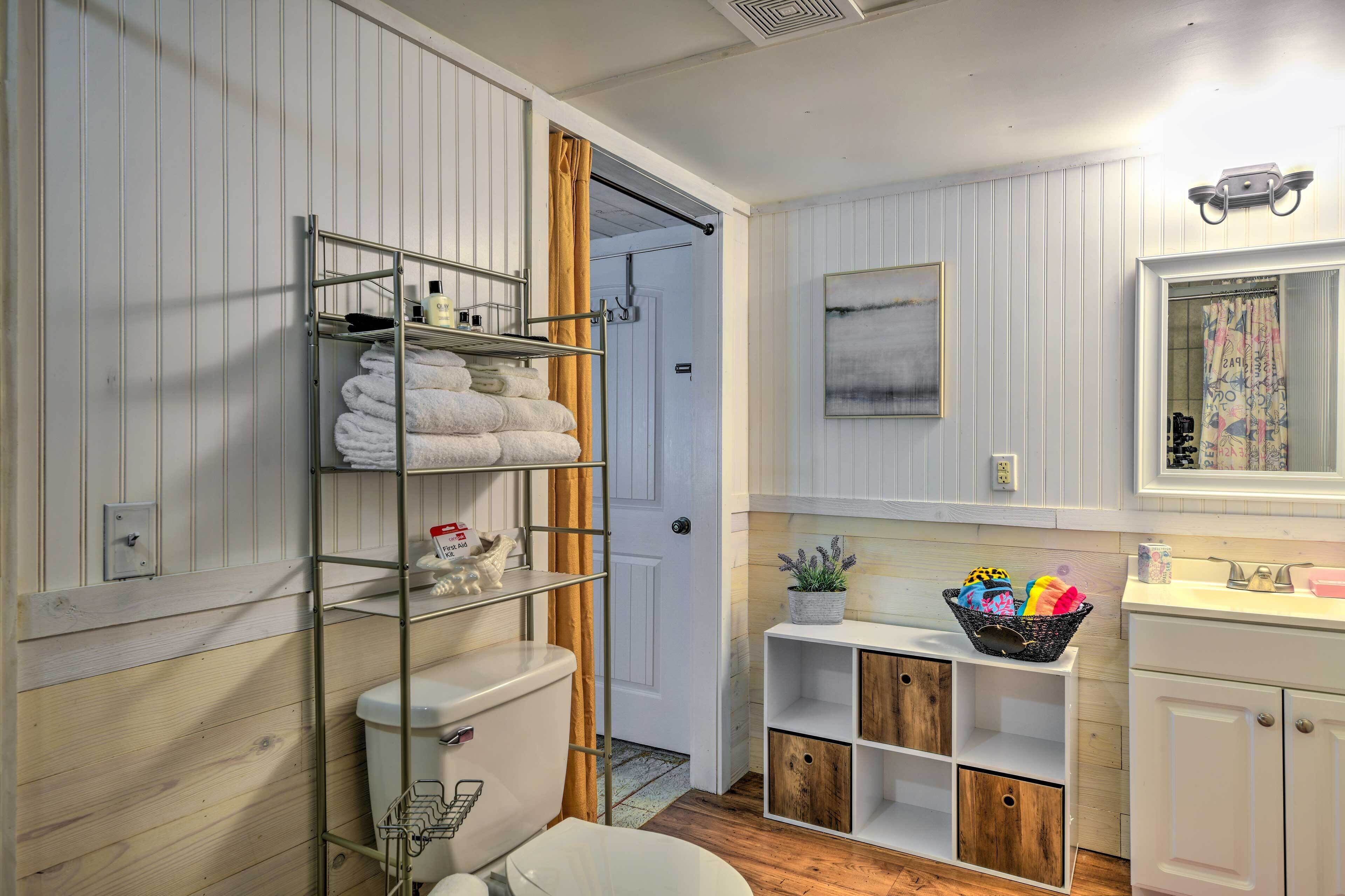 A bathroom with a white toilet, a metal towel rack with towels, a white sink, a mirror, and a shower area.