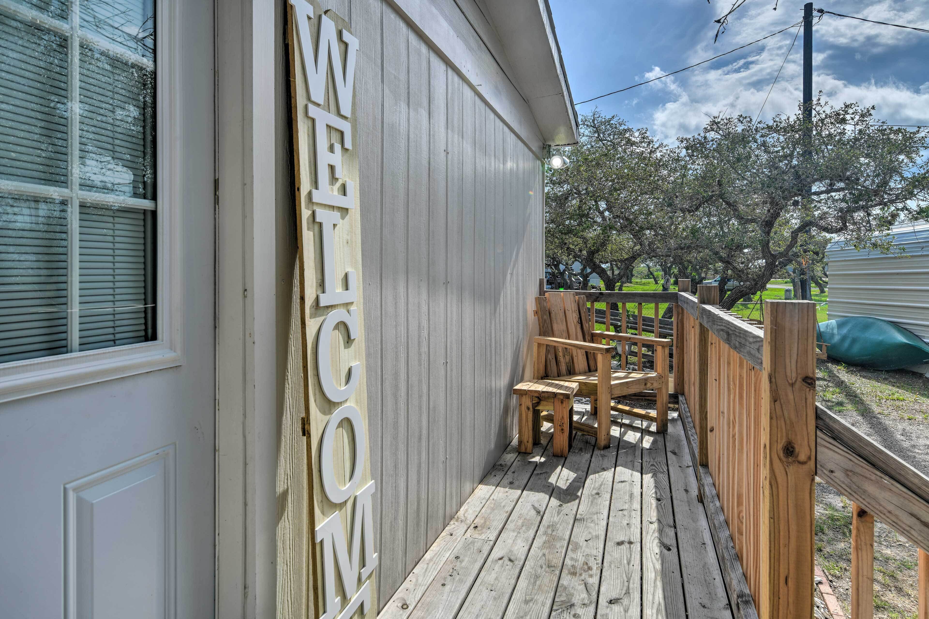 A wooden deck with a 'WELCOME' sign, a wooden chair, and a bench.