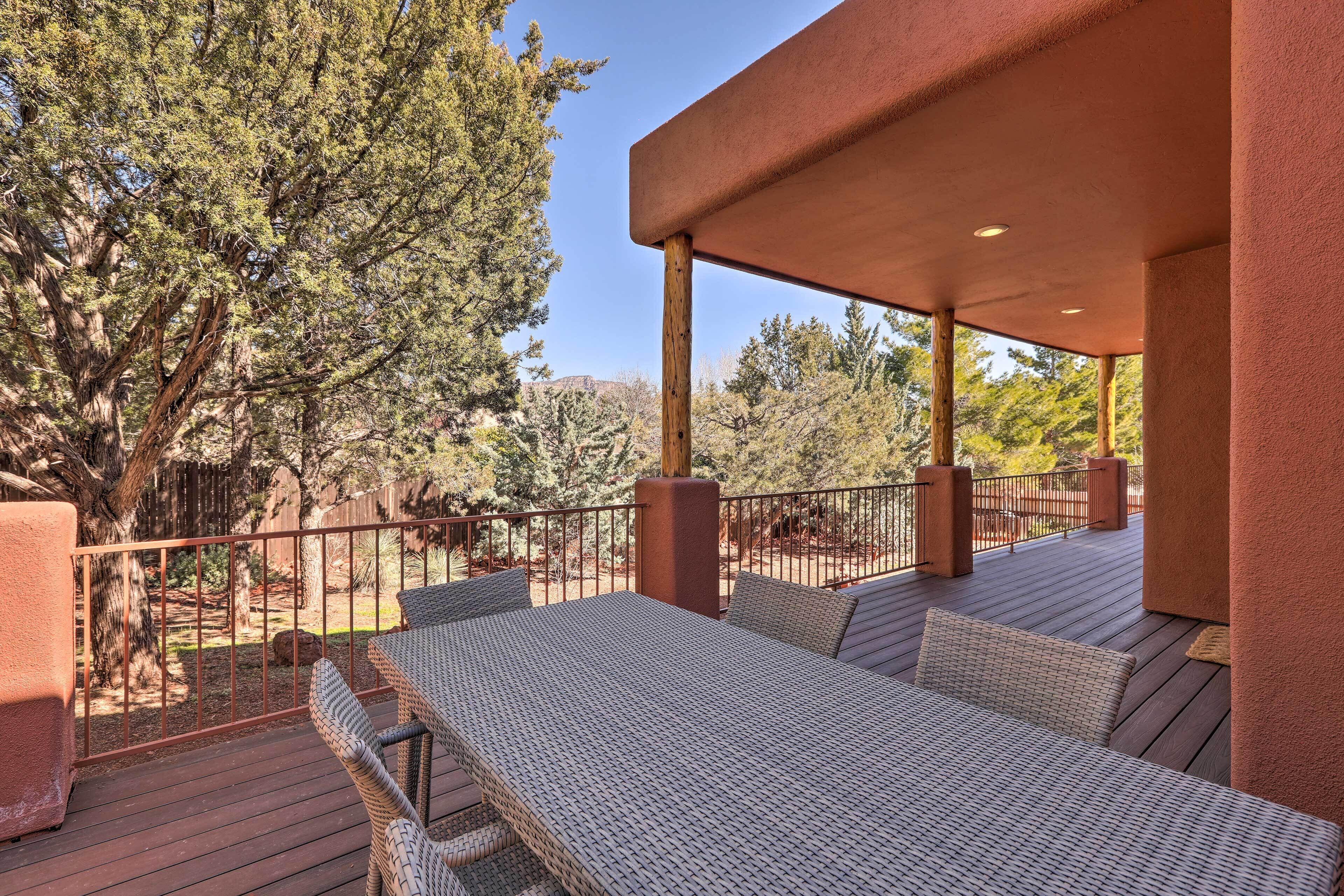A covered outdoor seating area with wicker furniture and a view of trees and a mountain in the background.