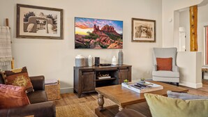 A living room with a wooden coffee table, leather sofa, and a white armchair. There are framed pictures on the wall and a small cabinet with decorative items. - Luxury Sedona Living: Remodeled w/ Red Rock Views! (Sedona)