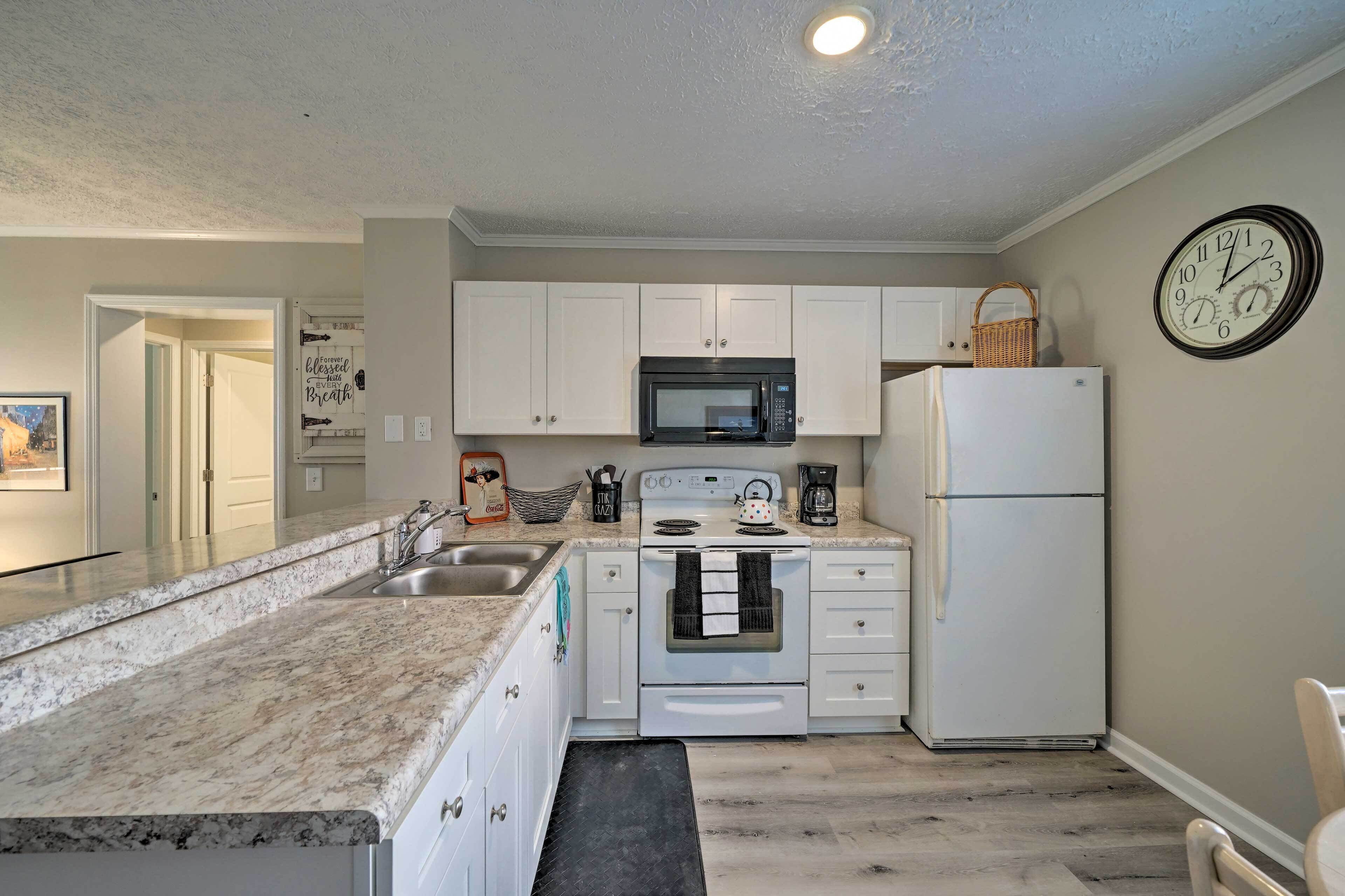 A kitchen with white cabinets, a microwave, a stove, a refrigerator, and a clock on the wall.