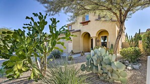 A desert-style house with arched doorways, surrounded by cacti and other desert plants. - Luxe Goodyear Home w/ Serene Backyard & Game Room (Goodyear)