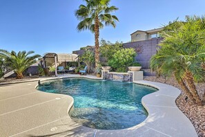 Una piscina de borde curvo, rodeada de palmeras y un patio con mobiliario exterior.