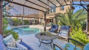 A covered outdoor area with a pool, lounge chairs, and a table with decorative items. - Luxe Goodyear Home w/ Serene Backyard & Game Room (Goodyear)
