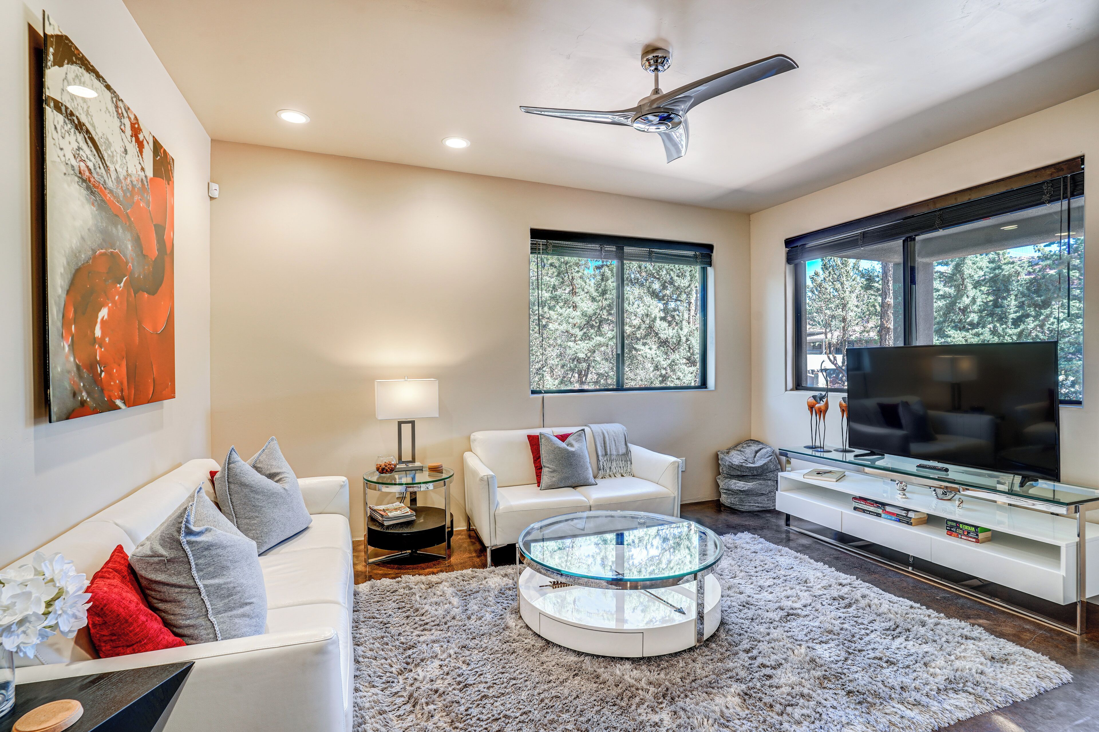 A modern living room with a white sofa, round glass coffee table, and a flat-screen TV.