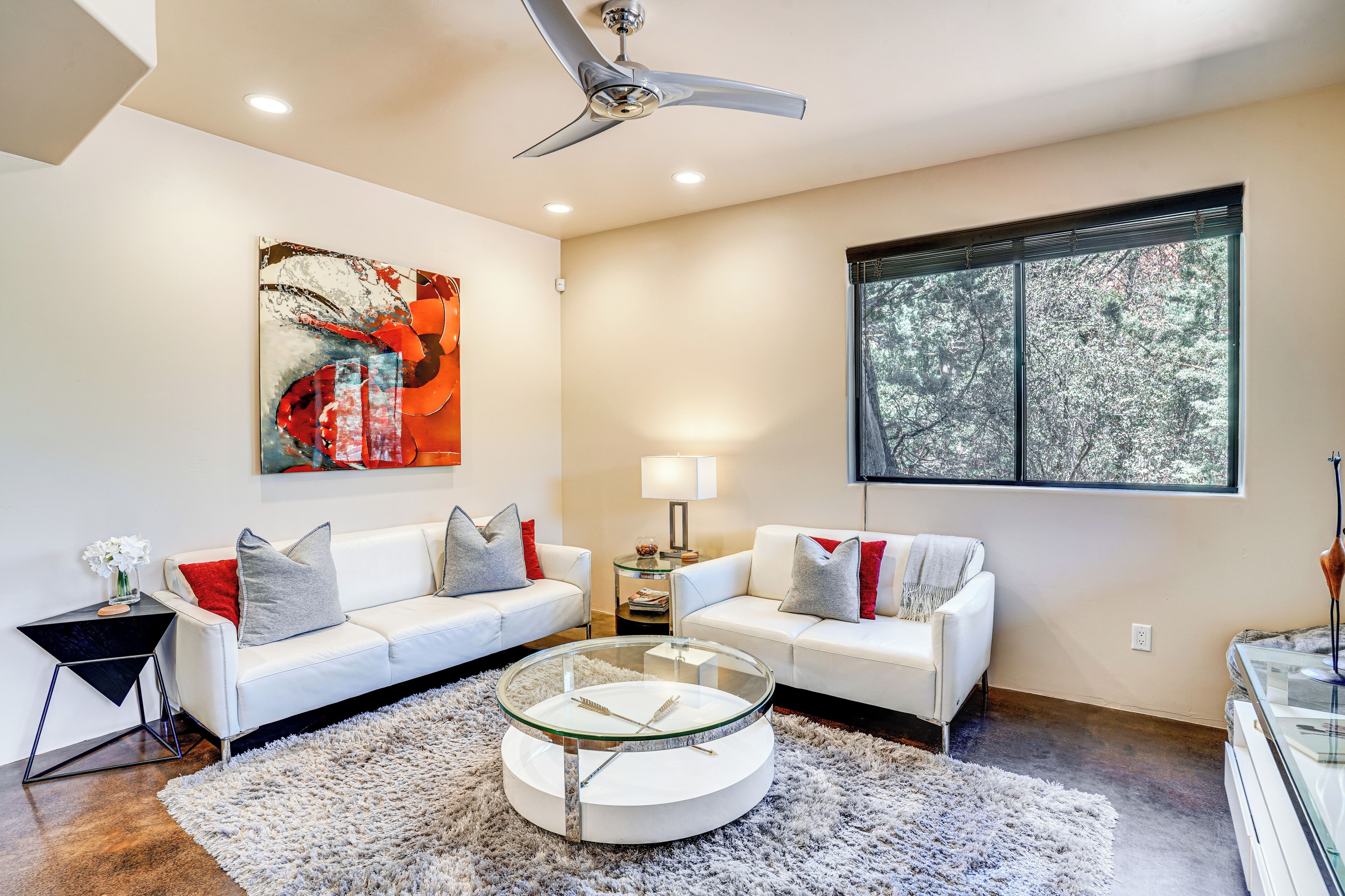 A modern living room with two white sofas, a glass coffee table, and a large abstract painting on the wall.