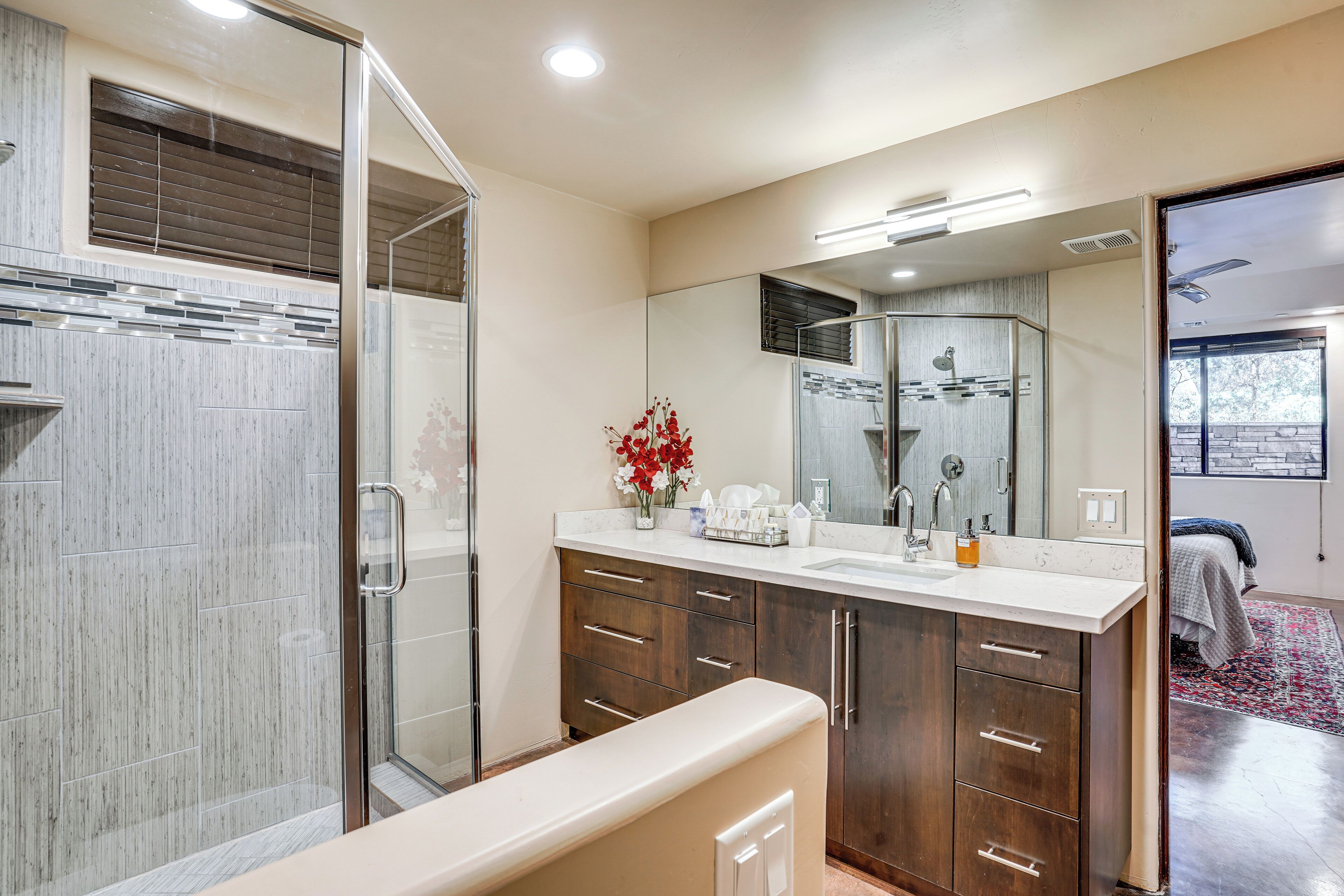 Un baño moderno con cabina de ducha de vidrio, un espejo grande y un tocador con varios cajones.