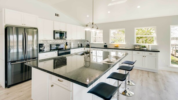 A modern kitchen with a central island, stainless steel appliances, white cabinetry, and bar stools. - Spacious San Jacinto River Home w/ Waterfront Deck (Houston)