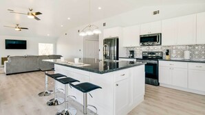 A modern kitchen with white cabinets, a central island with bar stools, a built-in oven, and a large window. - Spacious San Jacinto River Home w/ Waterfront Deck (Houston)