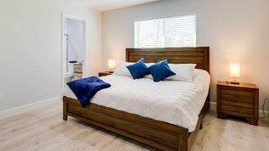 A bedroom with a wooden bed, white bedding, two blue pillows, bedside tables with lamps, and a window with blinds. - Spacious San Jacinto River Home w/ Waterfront Deck (Houston)