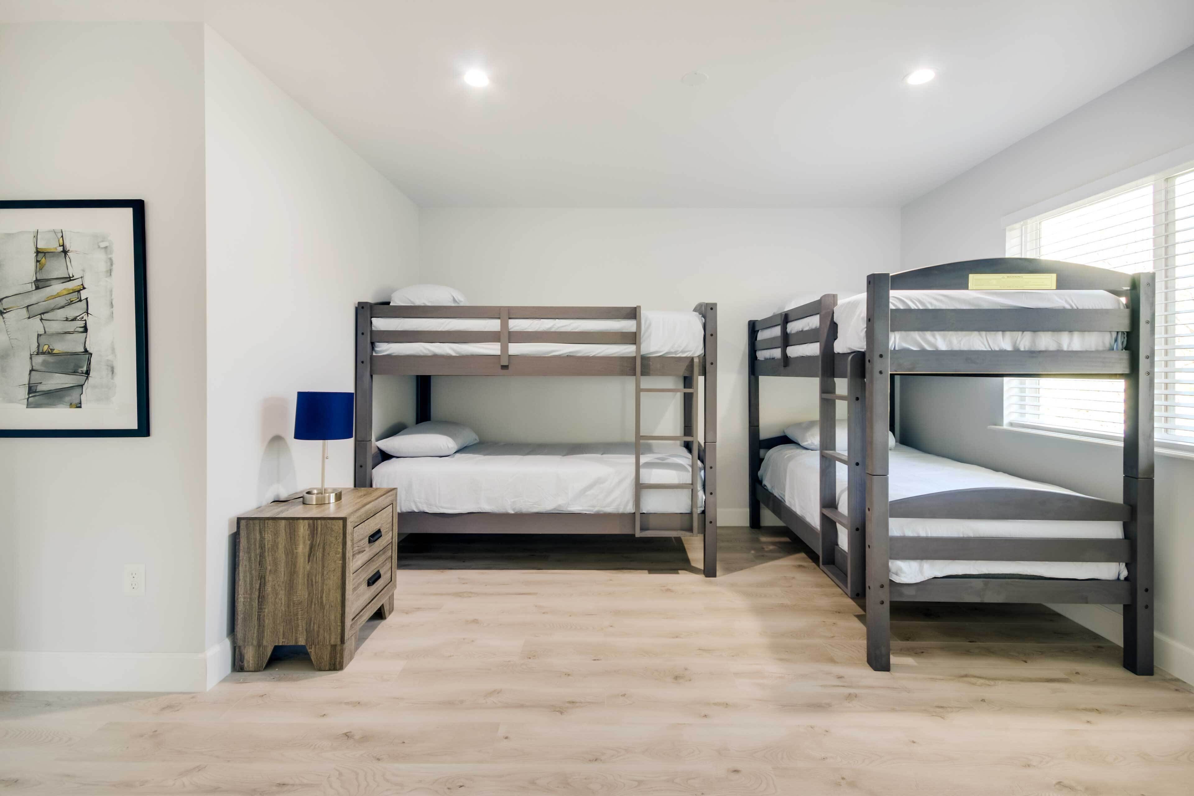 Una habitación con tres camas literas, una mesita de noche de madera, una lámpara y un cuadro en la pared.