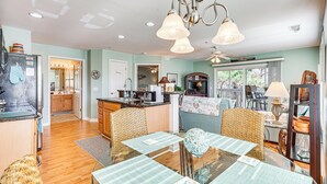 A spacious kitchen with wooden cabinets, a dining area with a glass table, wicker chairs, and a view of the backyard through large windows. - Marina & Beach Club Access: Condo in Southport (St. James)