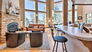 A spacious living area with a stone fireplace, large windows, a bar area, and a cozy seating arrangement. - Spacious Angel Fire Home w/ Deck & Resort Perks! (Angel Fire)