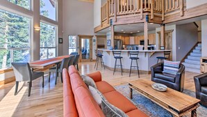 A spacious living area with a large wooden dining table, a red sofa, and a kitchen area with a wooden staircase. - Spacious Angel Fire Home w/ Deck & Resort Perks! (Angel Fire)