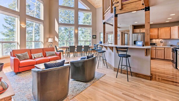 A spacious living area with a large window, a red sofa, and a kitchen with wooden cabinets and a bar area. - Spacious Angel Fire Home w/ Deck & Resort Perks! (Angel Fire)