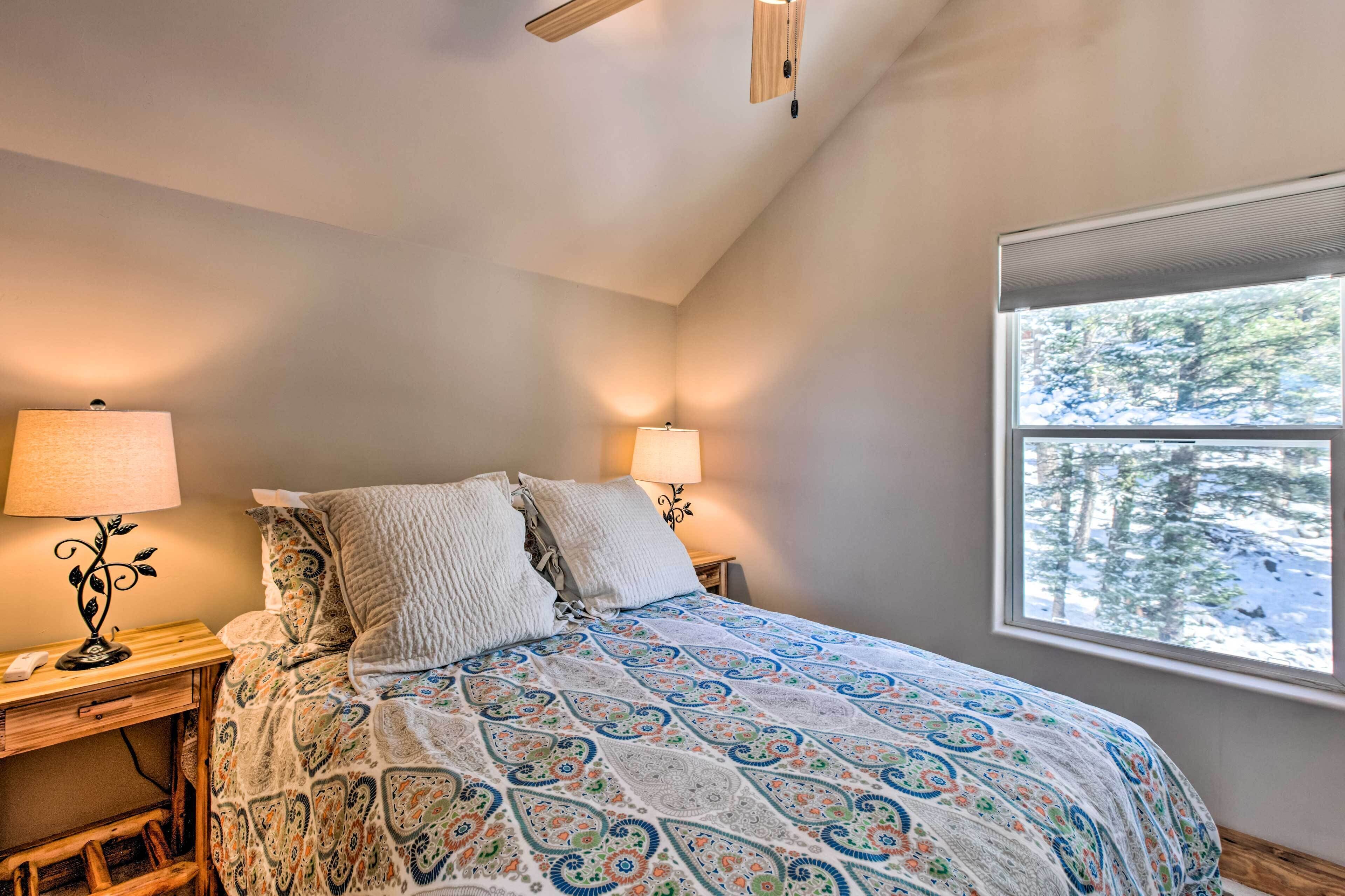 A bedroom with a bed, two bedside lamps, a window with a view of trees, and a wooden headboard.