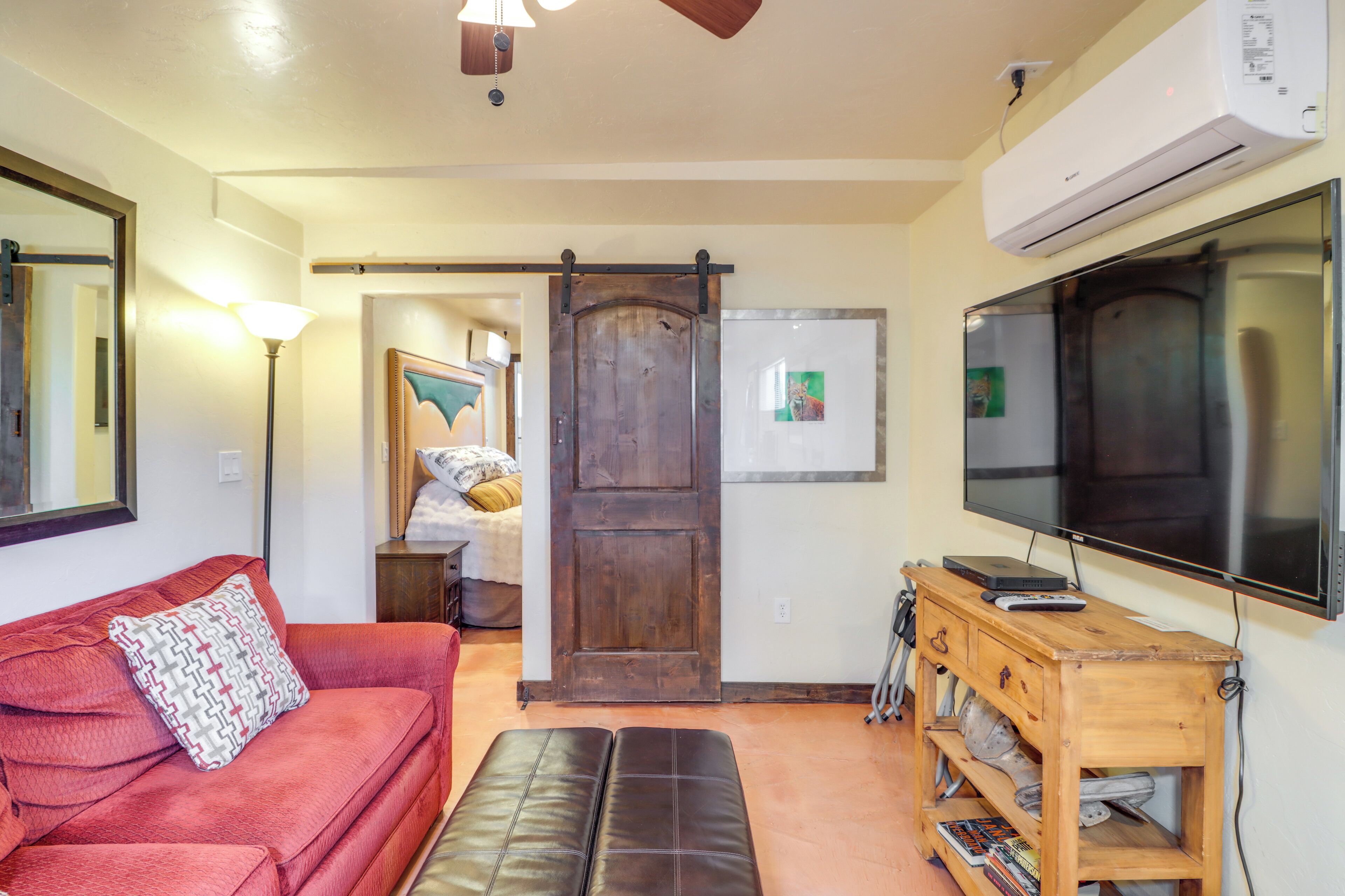 Una sala de estar con un sofá rojo, un banco de madera, un televisor y un puerta corredera.