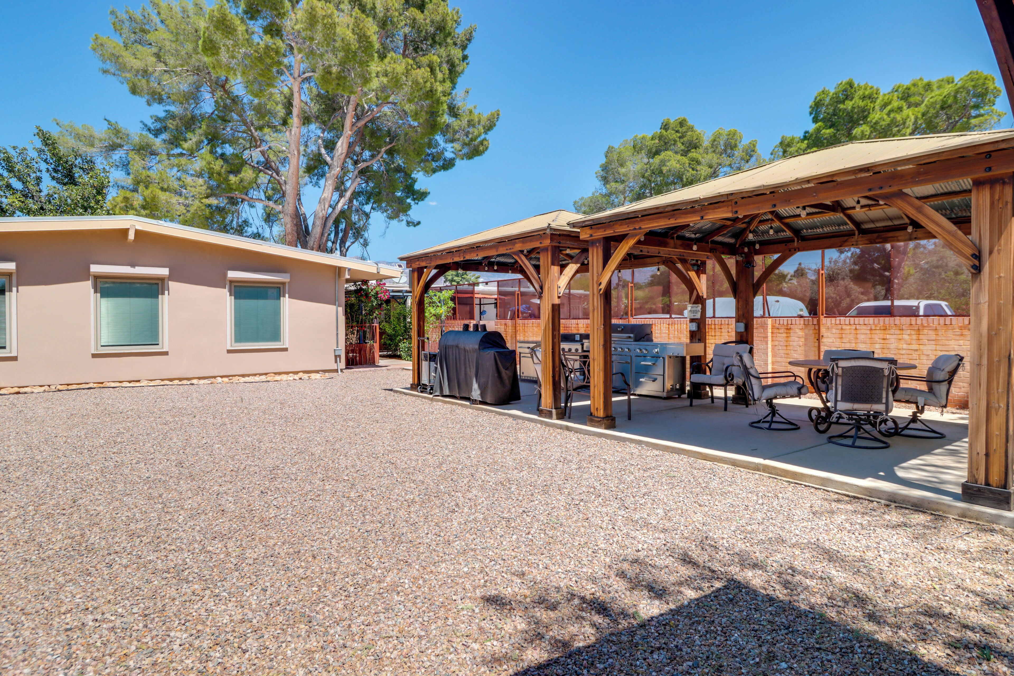A covered outdoor patio with seating, a barbecue grill, and a building with windows.
