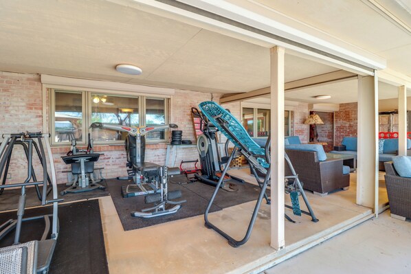 A gym with exercise equipment, a brick wall, and a seating area with blue cushions. - Pet-friendly Tucson Casita: Shared Swim Spa! (Tucson)