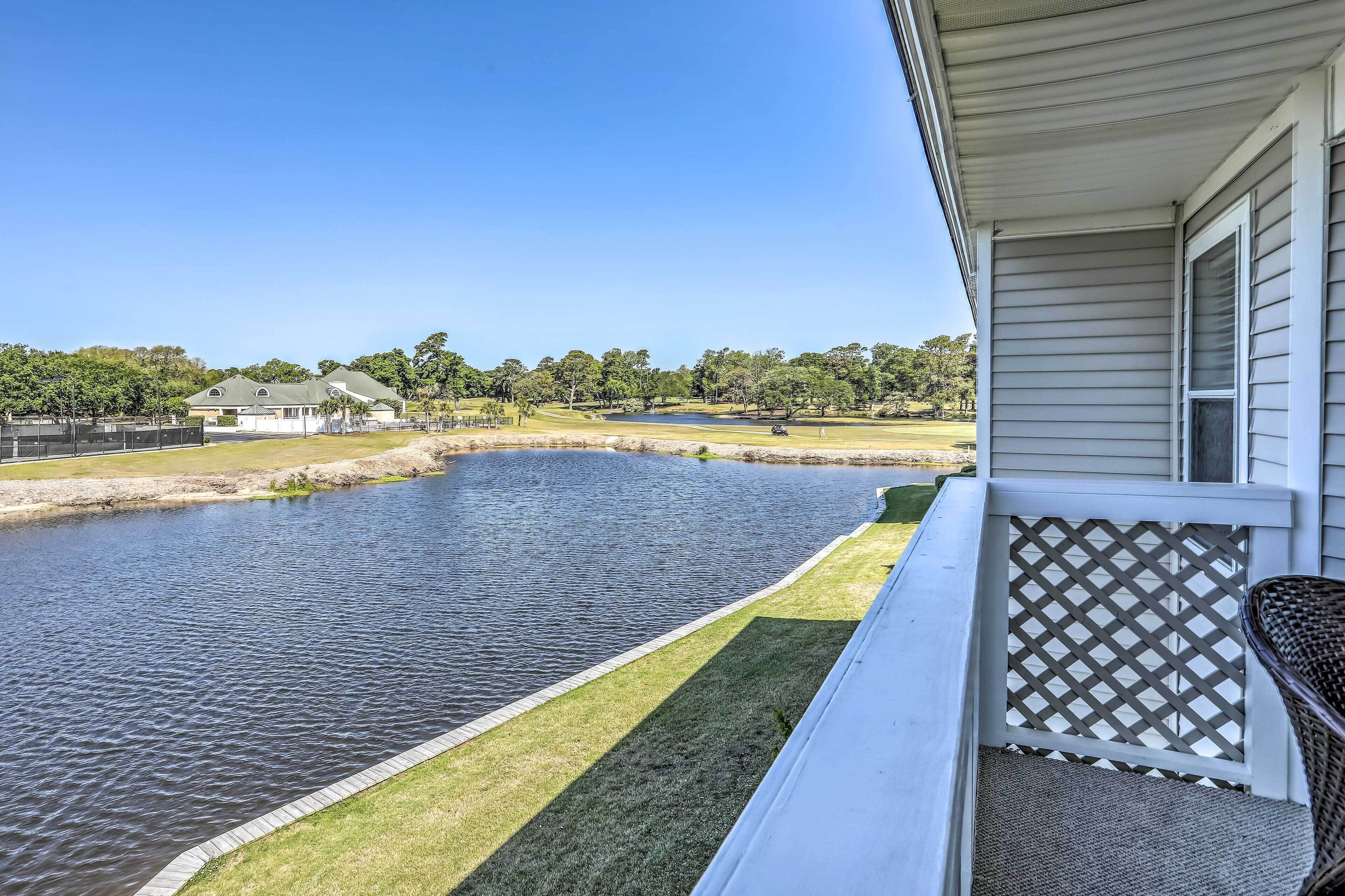 Propiedad residencial con vista a un estanque, césped y un campo de golf distante.