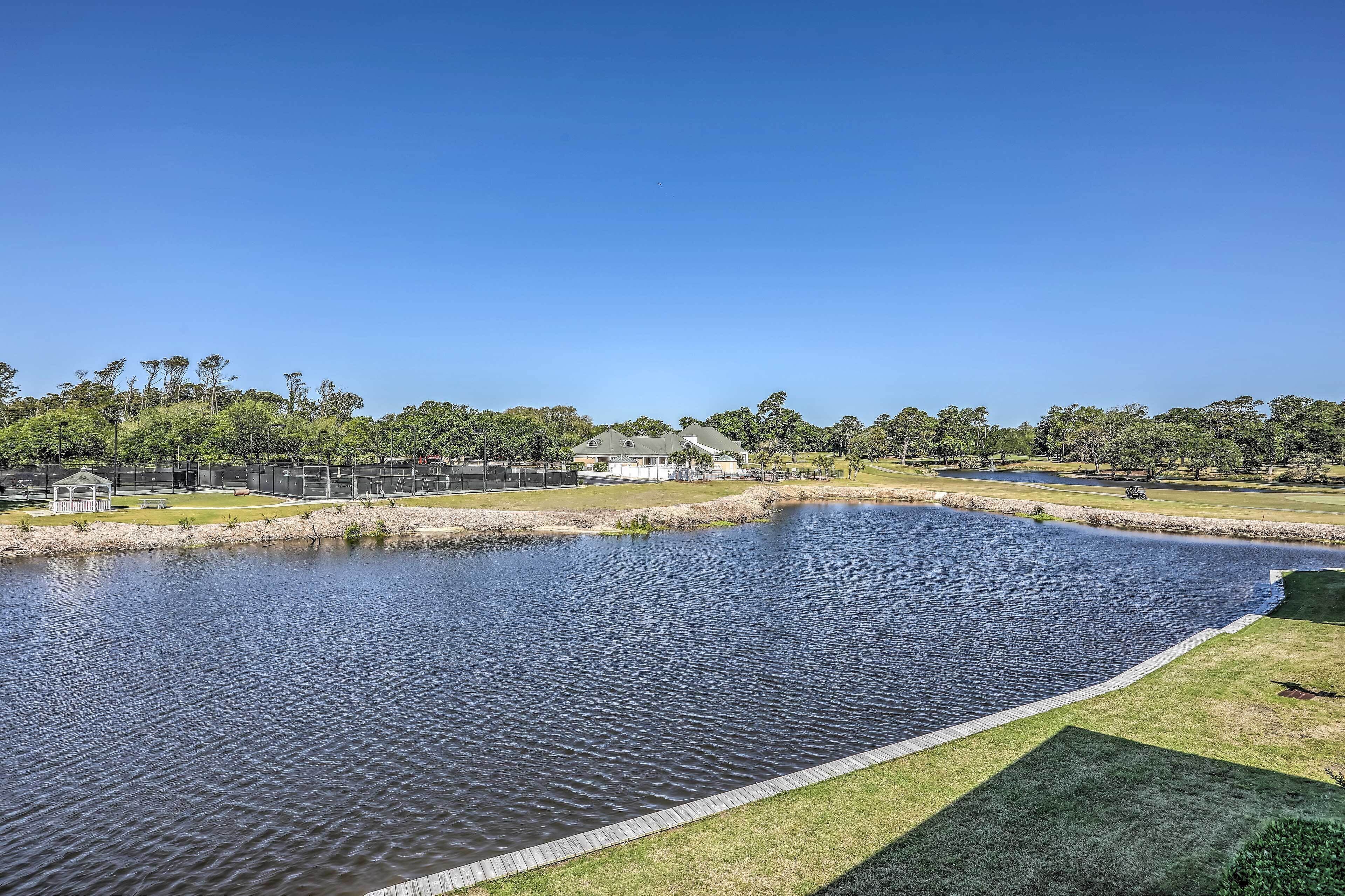 A large pond with a gazebo, surrounded by a fence and trees.