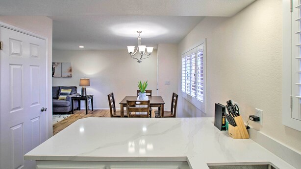 A modern kitchen with a marble island, wooden dining table, and chairs. There is a chandelier above the table and a window with blinds on the right. - Resort Perks, Course Views: Paradise Valley Condo! (Phoenix)