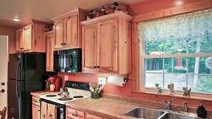 A kitchen with wooden cabinets, a black refrigerator, a stove, and a sink. - Secluded Birnamwood Cottage w/ Deck & River Views! (Birnamwood)