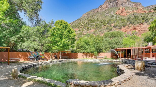 A swimming pool surrounded by a stone wall, with a wooden deck and a mountain backdrop.