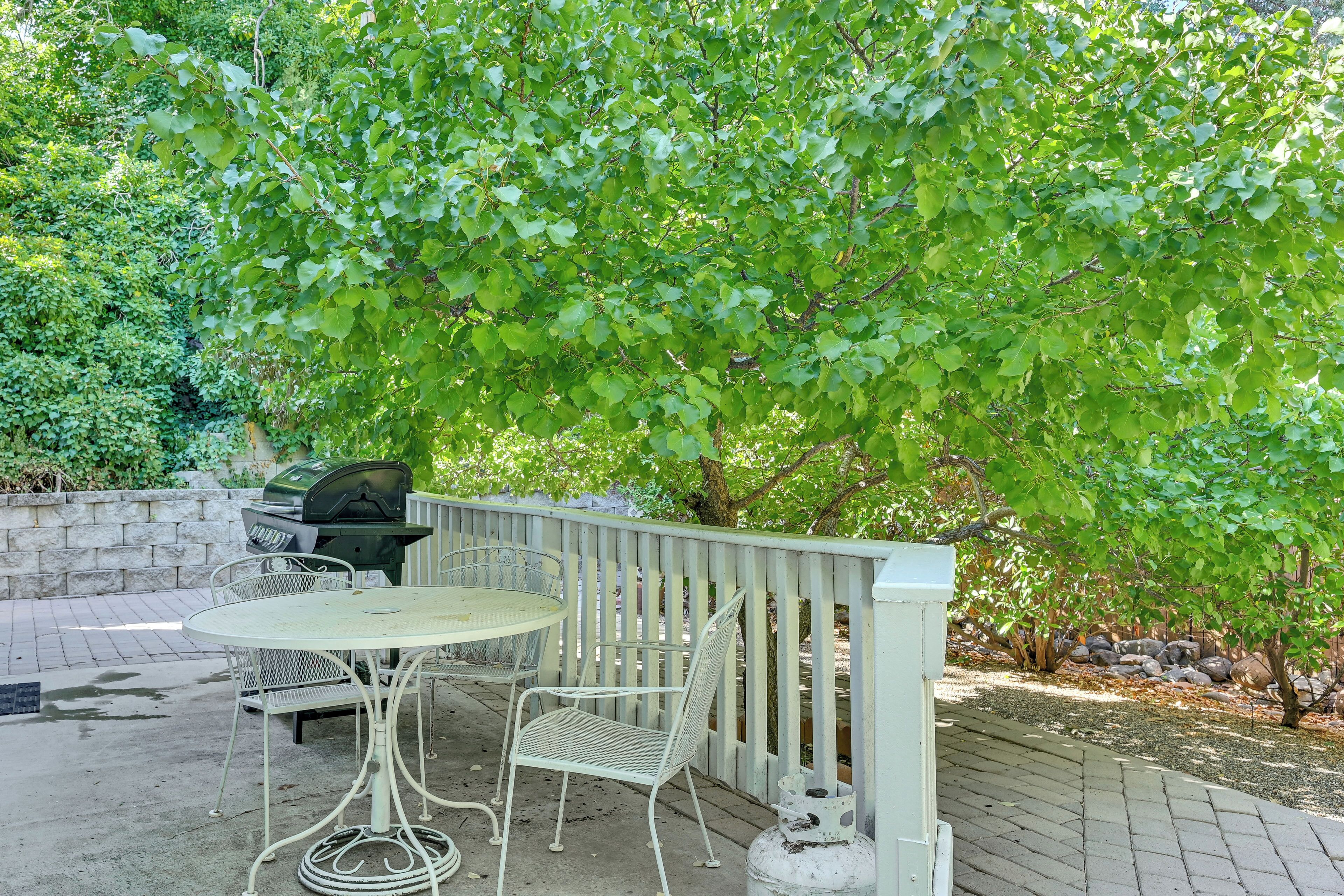 An outdoor patio with a round table and two chairs, a barbecue grill, and a white fence.