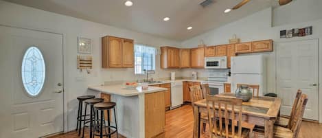 A kitchen with wooden cabinets, a central island, bar stools, a dining table with chairs, and a ceiling fan.