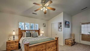 A bedroom with a wooden bed, two bedside tables with lamps, a ceiling fan, a window with blinds, and a door with a view.