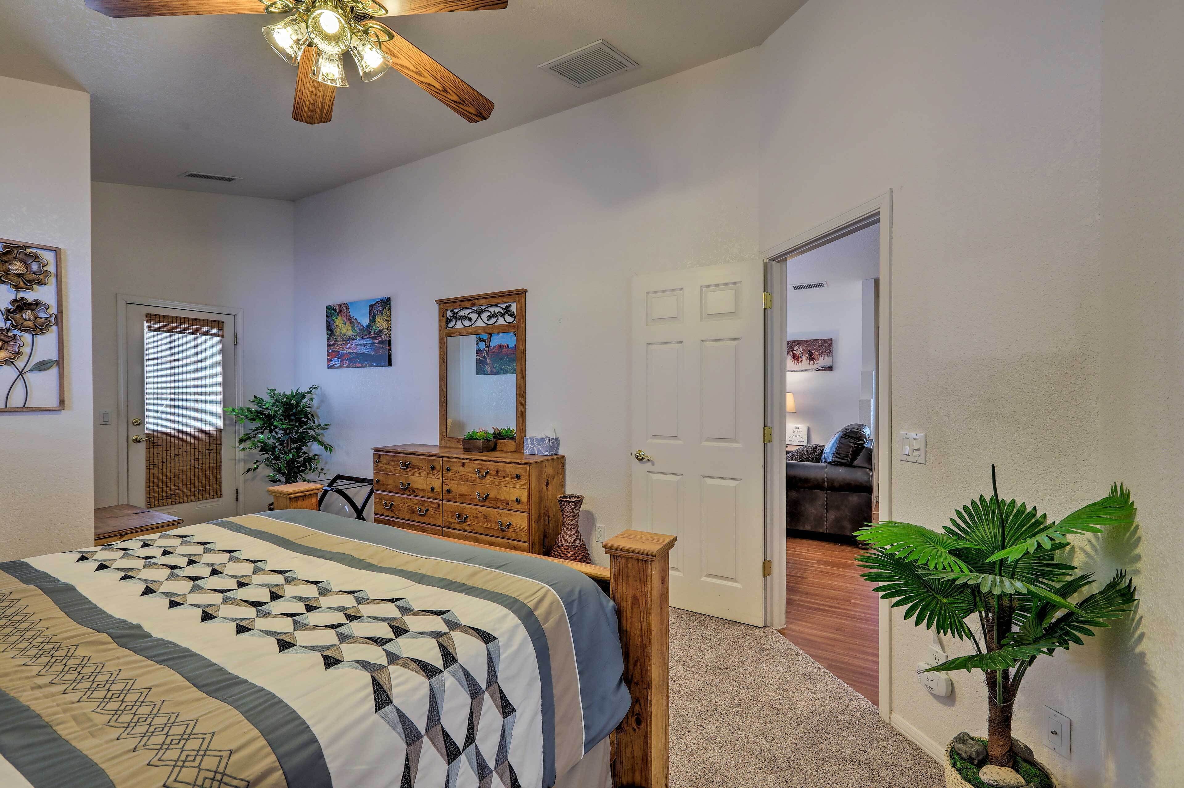 A bedroom with a bed, dresser, ceiling fan, and a potted plant.