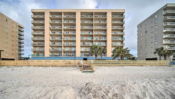 A multi-story hotel with balconies, a sandy beach in front, and palm trees. - Cozy Beachfront Escape w/ Pool & Gulf Access! (Gulf Shores)