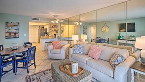 A spacious living room with a large mirror, a dining area with blue chairs, and a kitchen in the background. - Cozy Beachfront Escape w/ Pool & Gulf Access! (Gulf Shores)