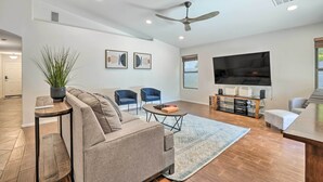Un salon moderne comprenant un canapé, deux fauteuils, une table basse, un téléviseur et un ventilateur de plafond.