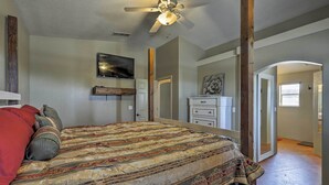 Quarto com cama grande, ventilador de teto, televisão e porta para outro cômodo.