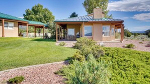 A two-story house with a covered patio, a well-maintained lawn, and a view of the surrounding landscape. - Zion Mountain Guest House w/ Canyon Vistas! (New Harmony)