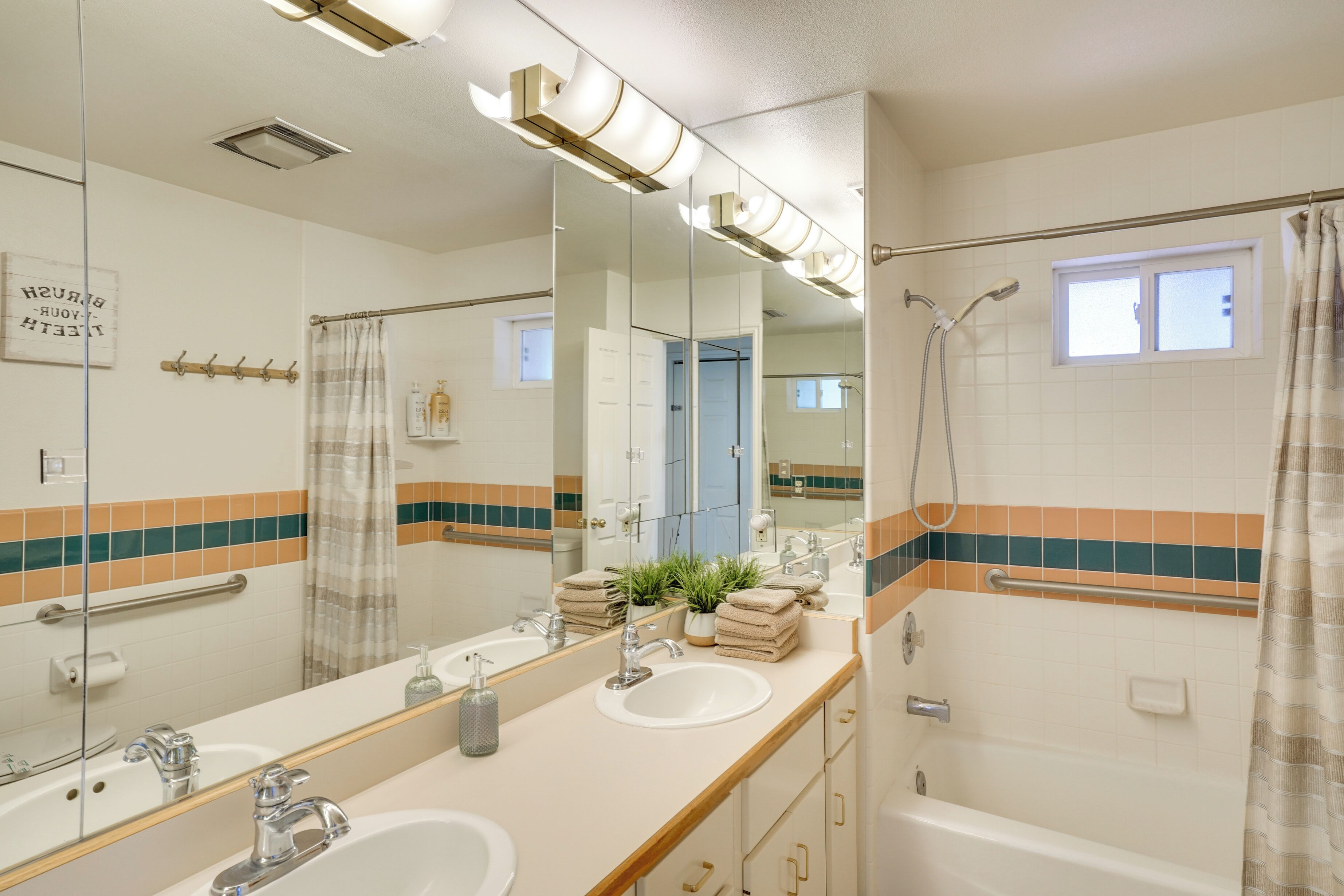 Un baño con un espejo grande, dos lavamanos, ducha y ventana.