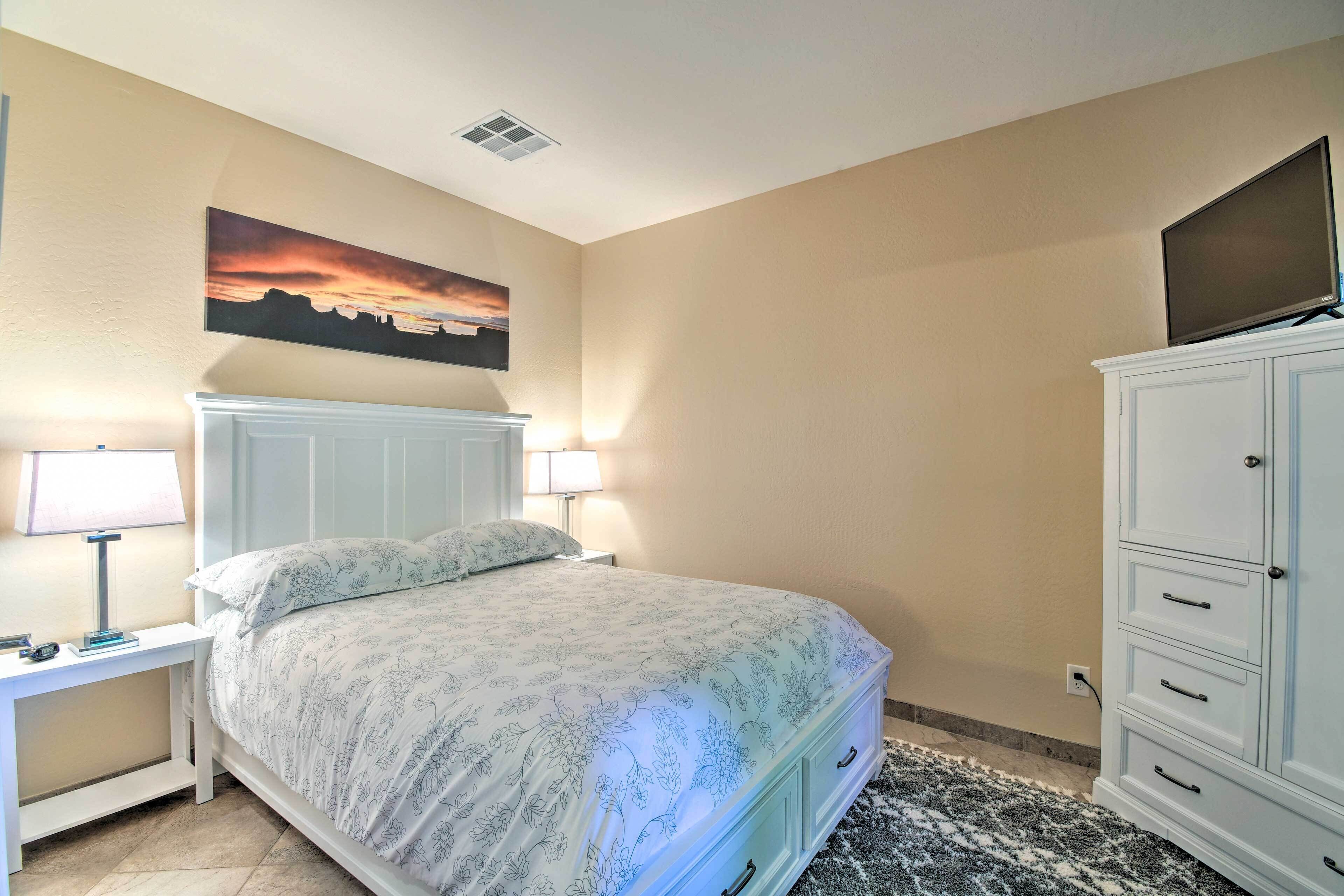 A bedroom with a bed, nightstands, a TV on a cabinet, and a painting on the wall.