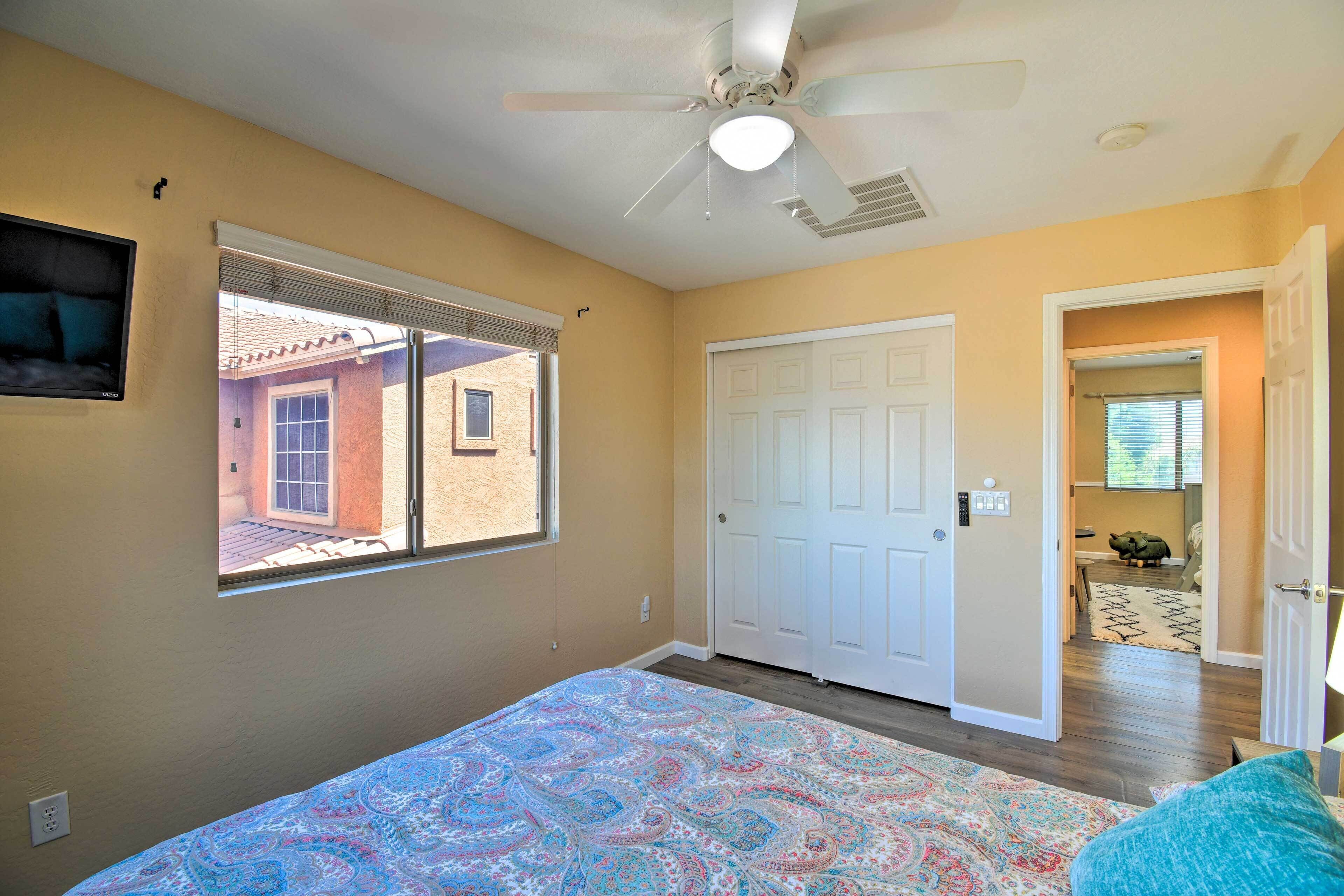A bedroom with a bed, a ceiling fan, a window, and a door leading to another room.