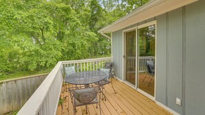 Une terrasse extérieure couverte, dotée d’une table et de chaises, entourée d’une clôture en bois et d’arbres.