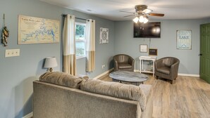 Un salon comprenant un canapé, deux fauteuils, une table basse, un ventilateur de plafond, un téléviseur et une carte accrochée au mur.
