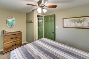 A bedroom with a bed, a dresser, a ceiling fan, a green door, and a framed picture on the wall.