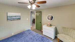 Une chambre à coucher comprenant un lit, une commode, une chaise, un ventilateur de plafond, une porte et un tableau accroché au mur.