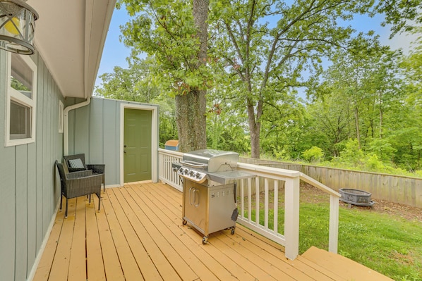 A wooden deck with a grill, a wicker chair, and a door.