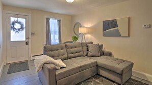 Ein Wohnzimmer mit Ecksofa, Stehlampe, Wandspiegel und einer Tür mit einem Kranz.