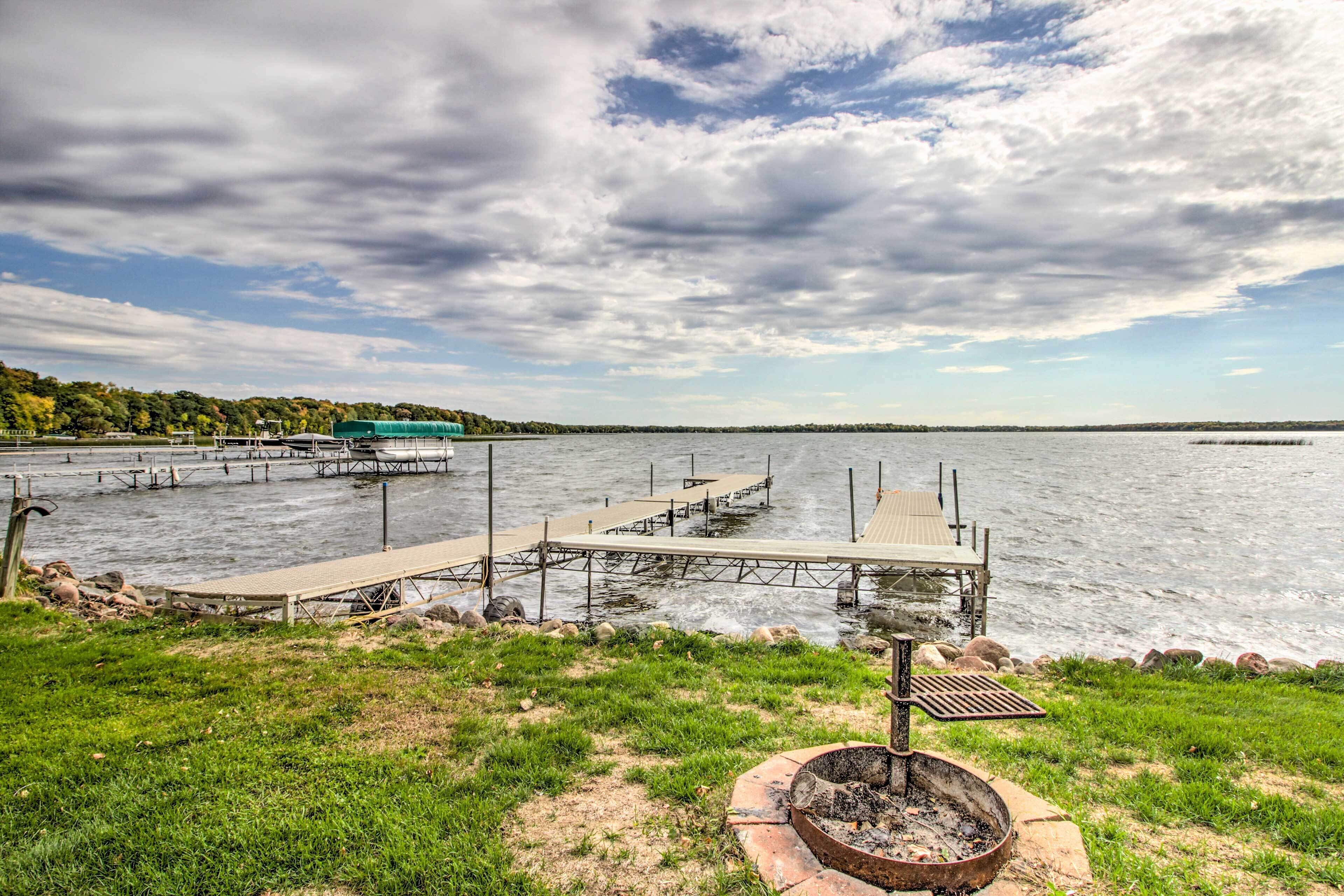A lakeside dock with a grassy area and a fire pit.