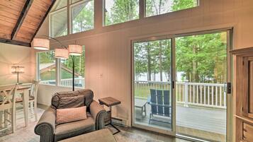 A spacious room with a large sliding glass door leading to an outdoor deck, a cozy seating area with a sofa and ottoman, and a small table.
